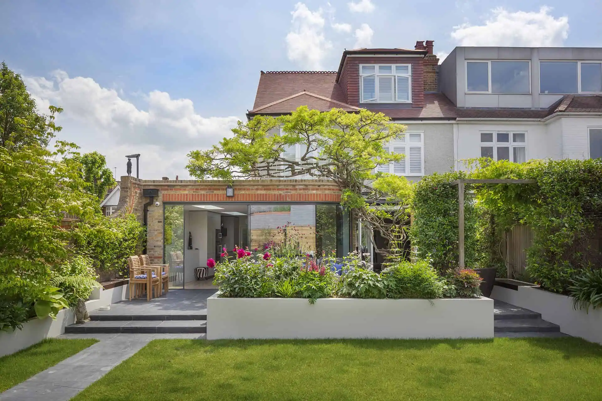 Luxury residential garden with modern extension, vibrant flowers, and greenery, showcasing high-end design and build services in Kensington by Convert Construction.