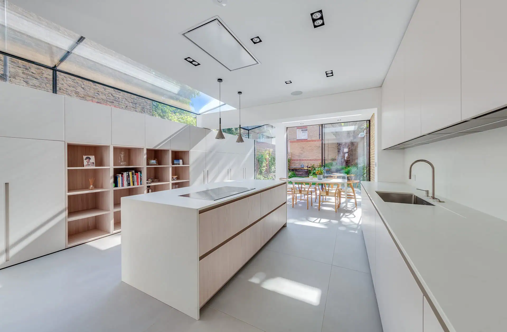 Modern kitchen extension featuring sleek cabinetry, an island with integrated cooktop, and large glass doors opening to a garden, showcasing luxury home extension design in Fulham.