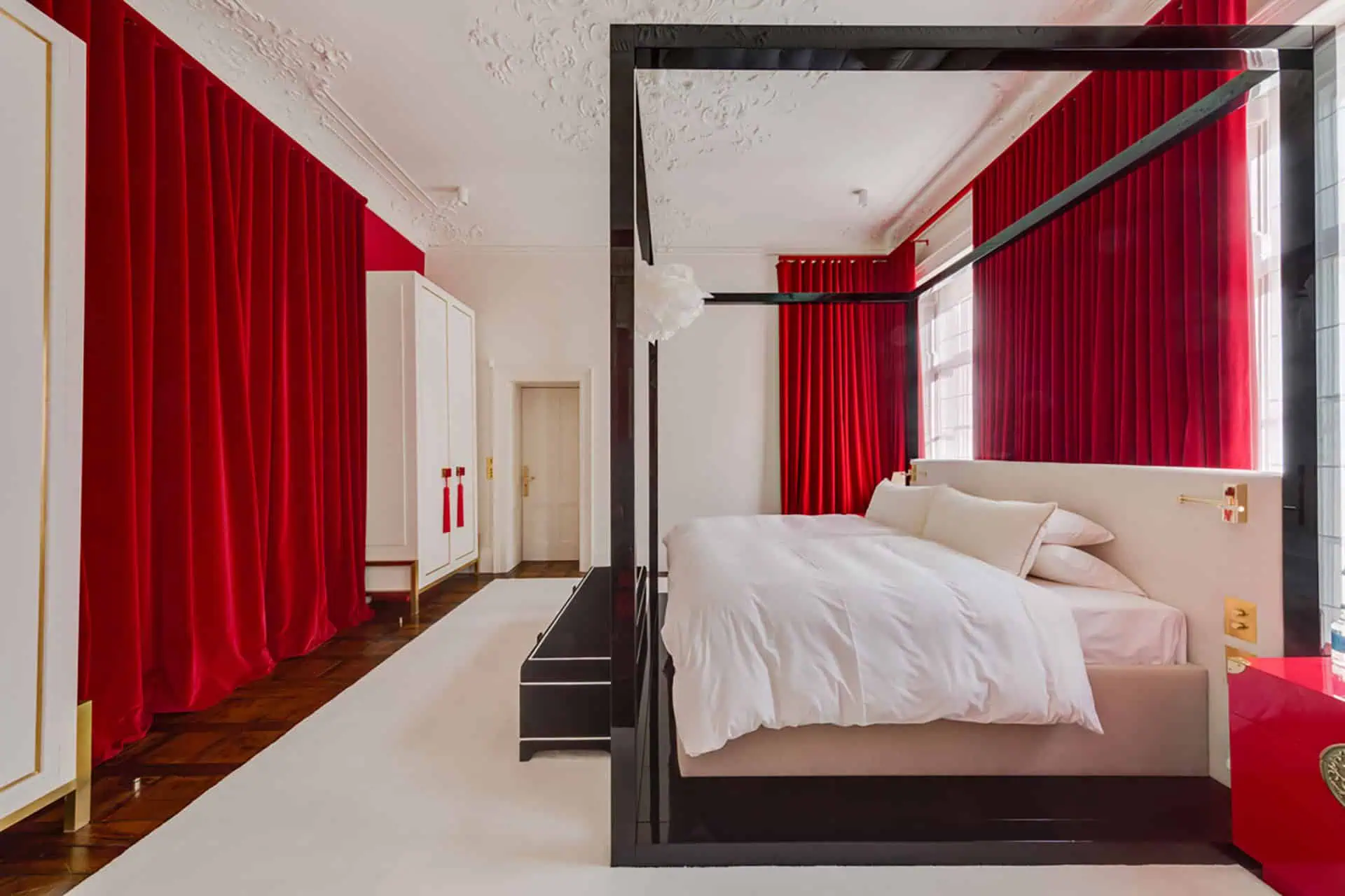 Luxury bedroom interior featuring a four-poster bed with white bedding, red velvet curtains, and elegant decor, showcasing high-end design suitable for luxury home refurbishments in Fulham.