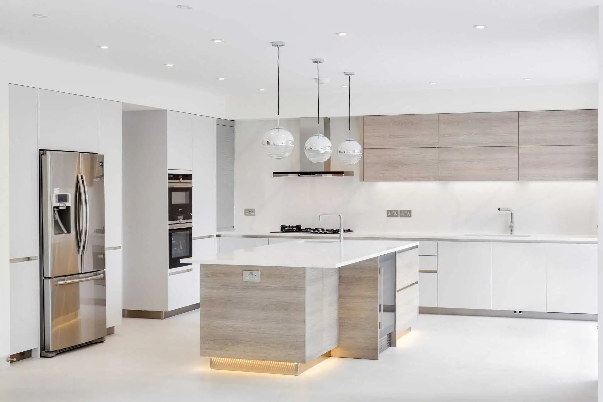 Modern luxury kitchen featuring sleek white cabinetry, high-end appliances, a central island with a wood finish, and stylish pendant lighting, exemplifying contemporary design in Kensington's new builds.
